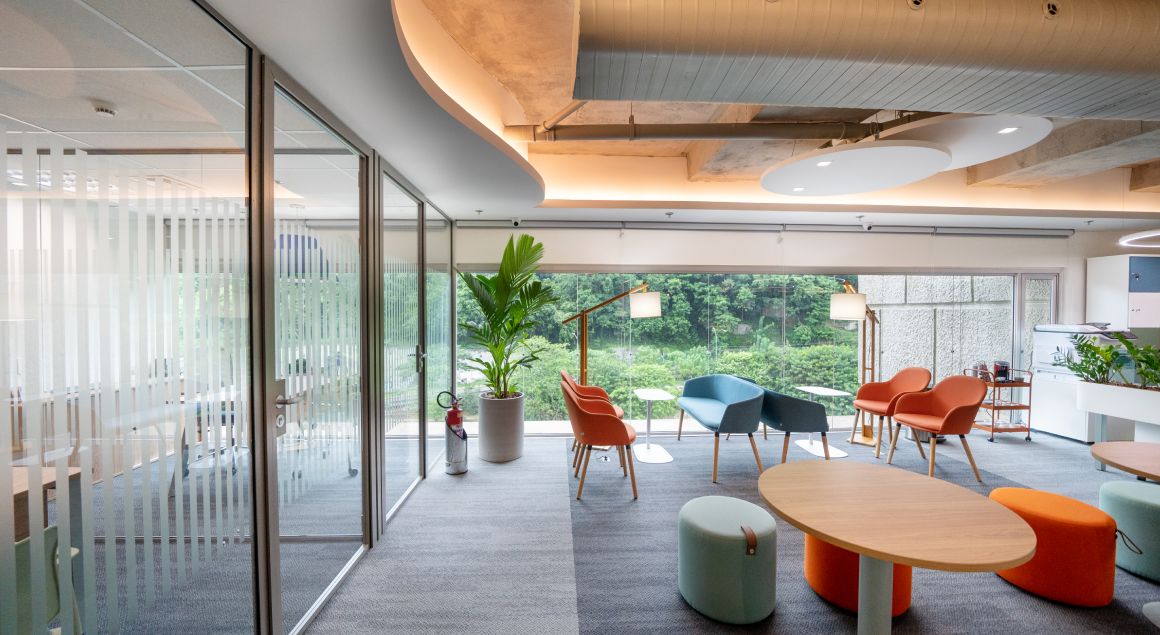 Modern office with colorful furniture, natural light, views of green areas and exposed ceiling with industrial style.