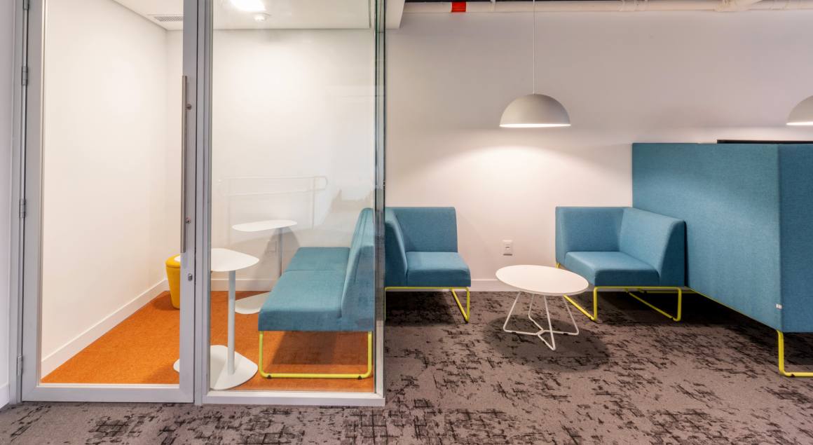 Living area in corporate office with blue armchairs and white coffee tables, lit by pendant lights